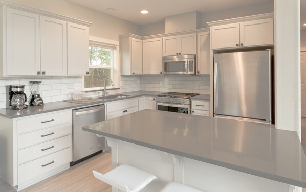 A modern kitchen with white cabinetry, stainless steel appliances, and a large island.