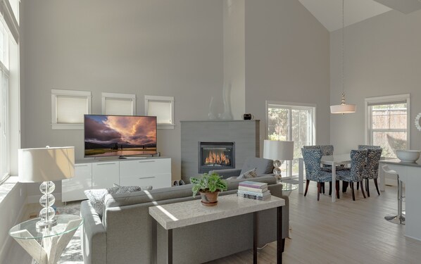 Una sala de estar moderna con chimenea, televisor de pantalla plana, sofá, mesa de centro y sillones estampados.