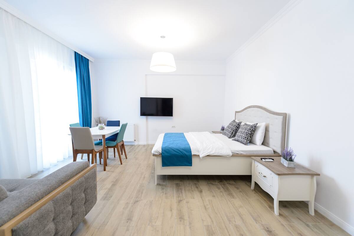 A hotel room with a bed, bedside table, TV, and a dining area with chairs and a table.