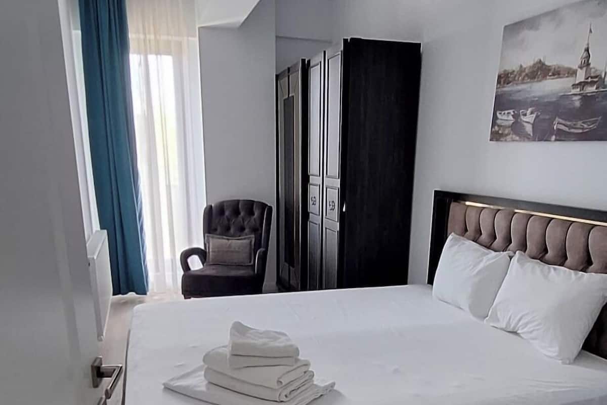 A hotel room with a large bed, a chair, a wardrobe, and a painting on the wall.