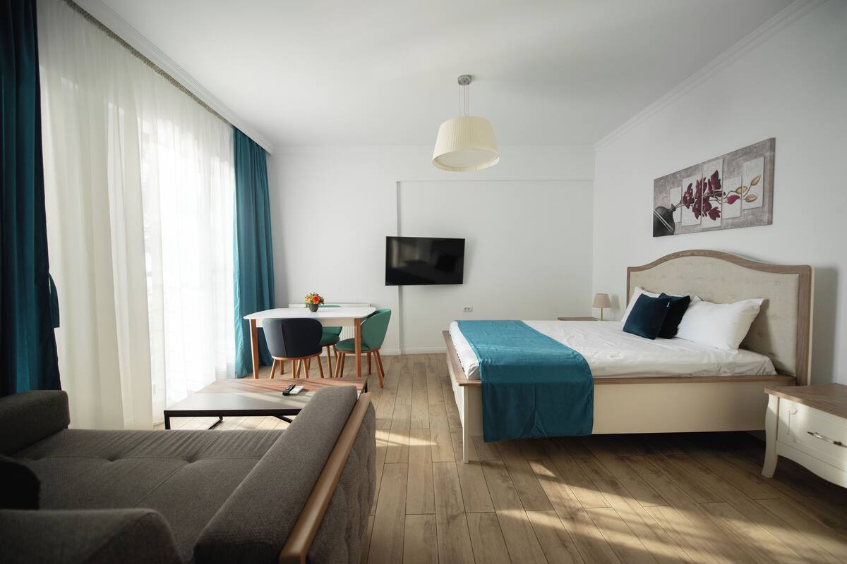 A modern hotel room with a bed, a desk, a chair, and a TV on the wall.