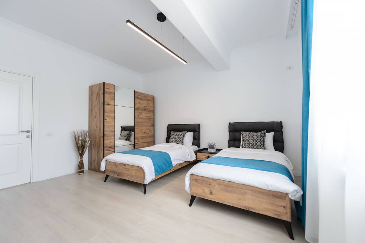A modern bedroom with two beds, a wooden wardrobe, a mirror, and a ceiling light.