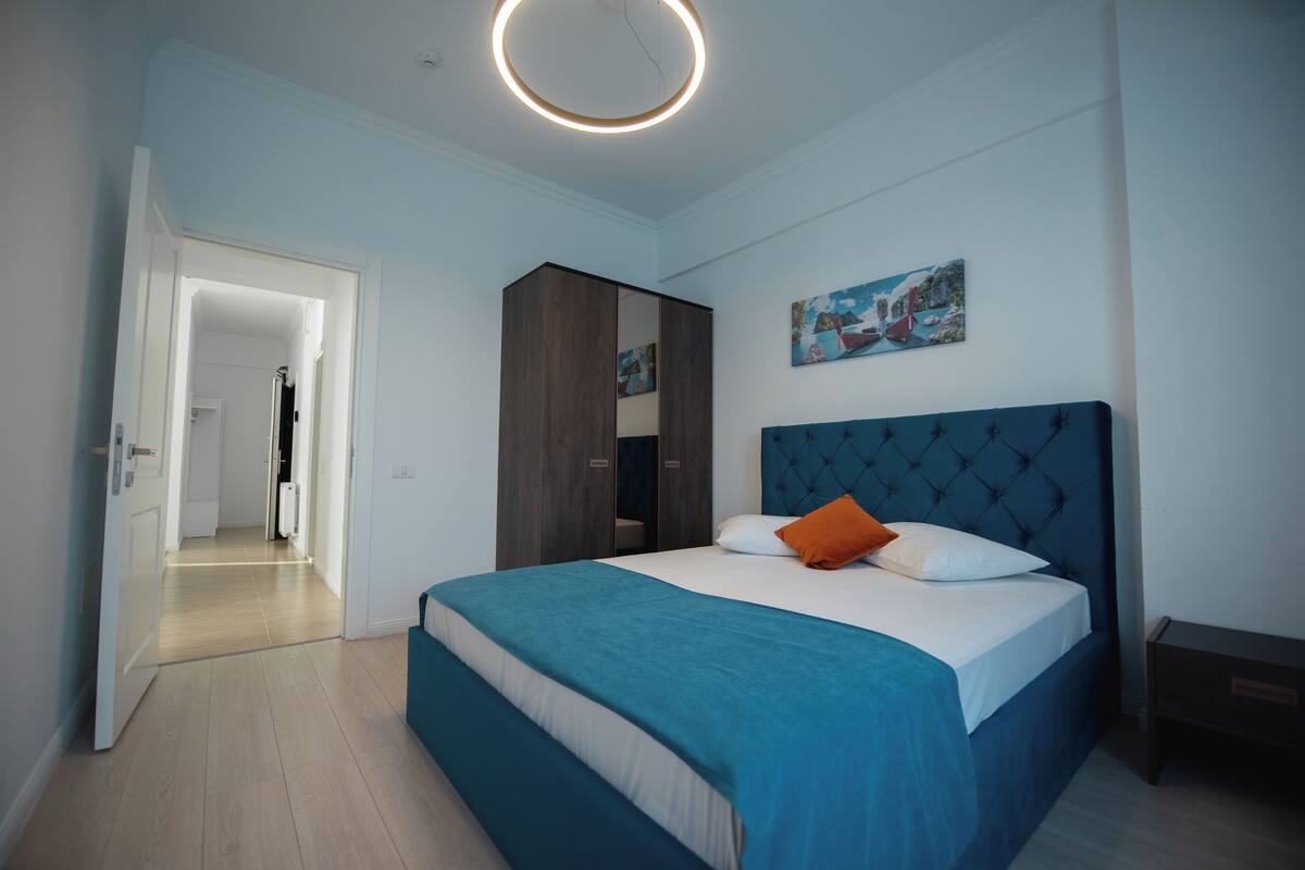 A modern bedroom with a large bed, a wardrobe, and a painting on the wall.