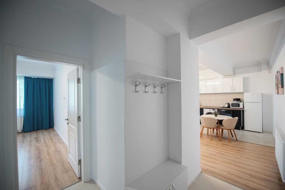 A modern kitchen with white cabinets, a dining area with two chairs, and a hallway with a blue curtain.