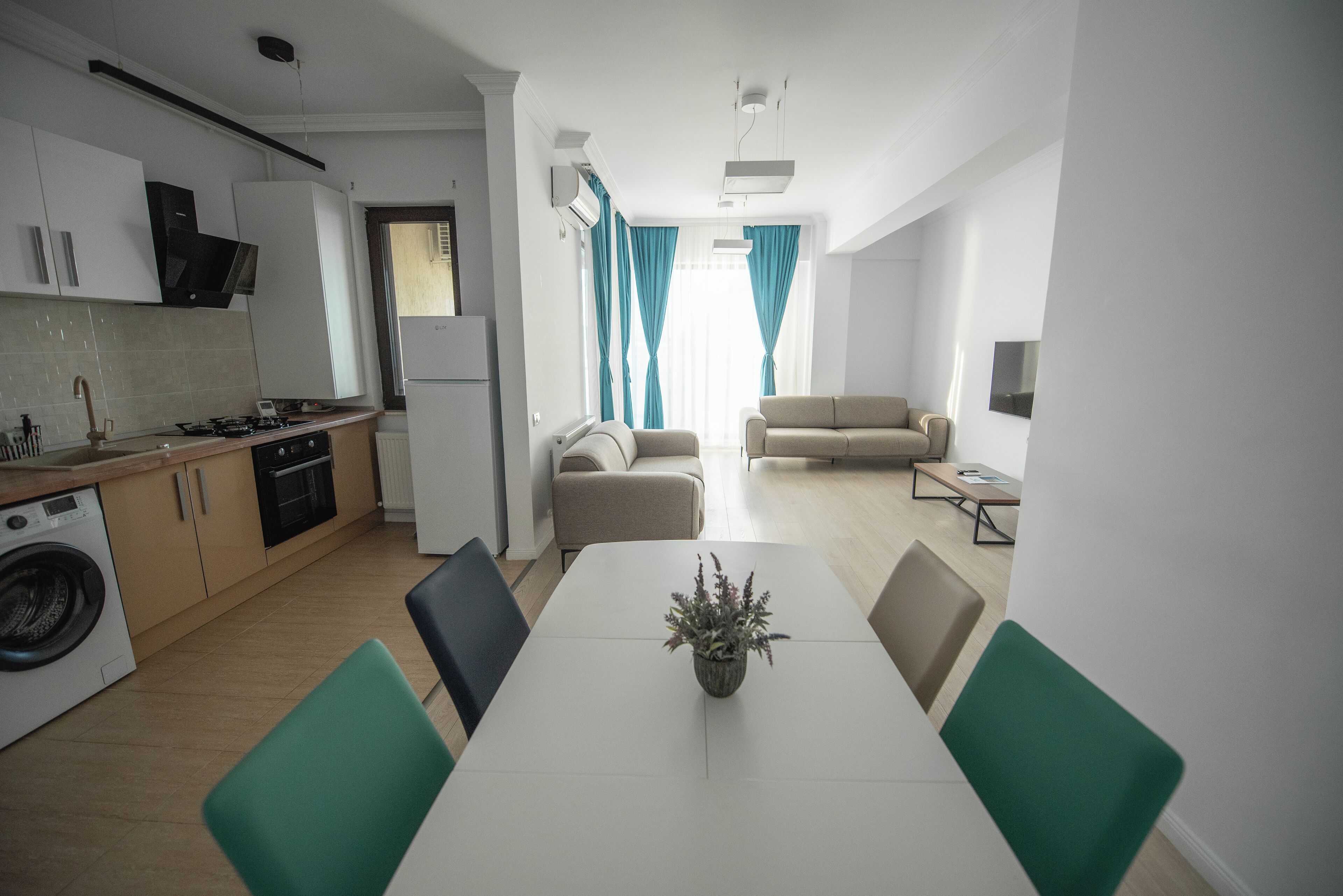 A modern kitchen with a dining area, a sofa, and a TV.