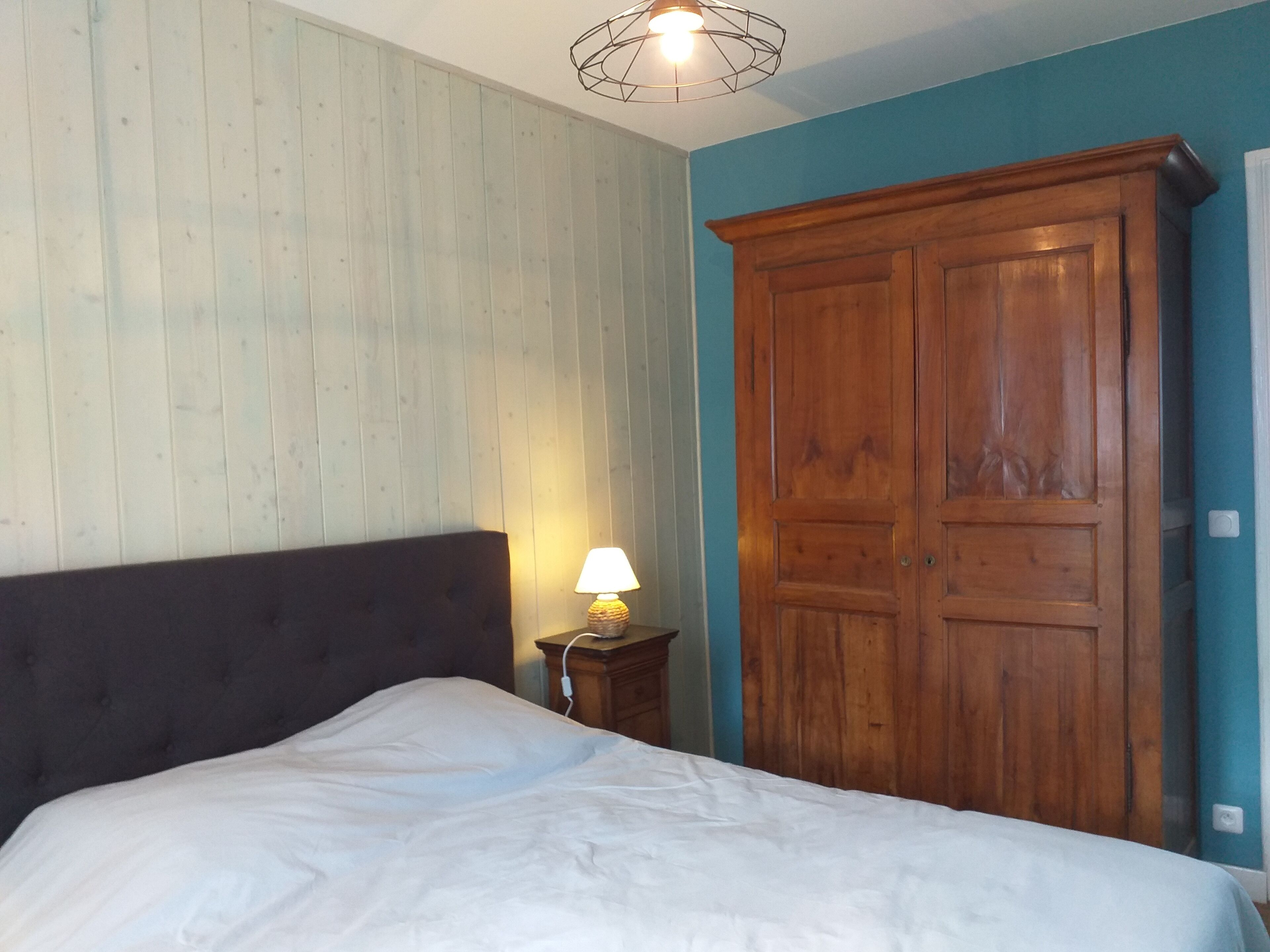 Ein Schlafzimmer mit einem Bett, einem Holzschrank, einem Nachttisch mit Lampe und einer Deckenleuchte.