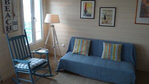 Una habitación con un sofá azul, almohadas a rayas, un sillón mecedor azul, una lámpara de pie y una pared con cuadros.