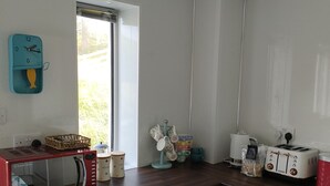 Een keuken met witte kasten, een magnetron, een broodrooster en een raam met uitzicht op groen.