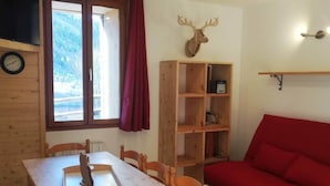 Una mesa de comedor de madera con sillas, un sofá rojo, una estantería de madera, un reloj de pared y una decoración con cabeza de venado.