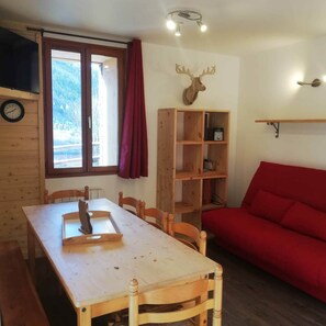 Ein Holztisch mit Stühlen, ein rotes Sofa, ein Holzregal, eine Wanduhr und eine Dekoration mit Hirschgeweih.