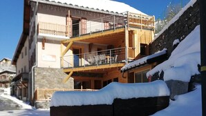 Un edificio de varios pisos con balcón de madera, escalones cubiertos de nieve y una pared de piedra.
