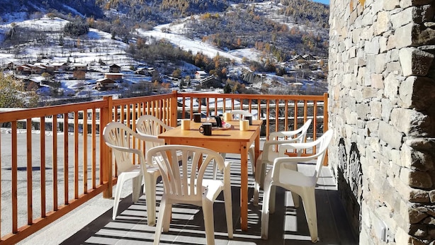 Balcón con mesa y sillas con vistas a un paisaje nevado de montañas.