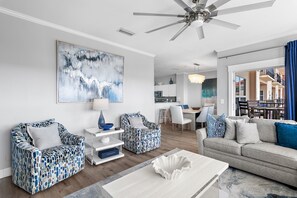 Un salon moderne doté d’un ventilateur de plafond, d’un grand tableau abstrait et d’un coin repas offrant une vue sur l’extérieur.