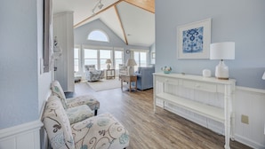 A spacious room with a high ceiling, a white bench, a lamp, and a framed artwork on the wall. - 7048- Tide Song - Dog-Friendly Oceanfront Rodanthe Retreat (Rodanthe)