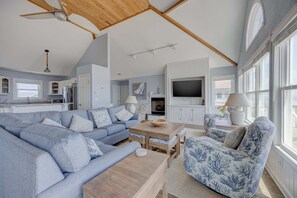 Uma sala de estar espaçosa com um sofá grande, uma poltrona azul menor, uma mesa de centro de madeira e uma televisão.