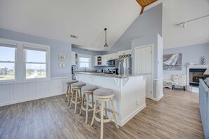 Une cuisine avec un coin bar, des tabourets en bois, une vue dégagée grâce à de grandes fenêtres et une cheminée.