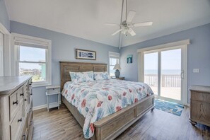 Quarto com cama, cômoda, mesa de cabeceira e vista para a praia através de uma porta de correr.