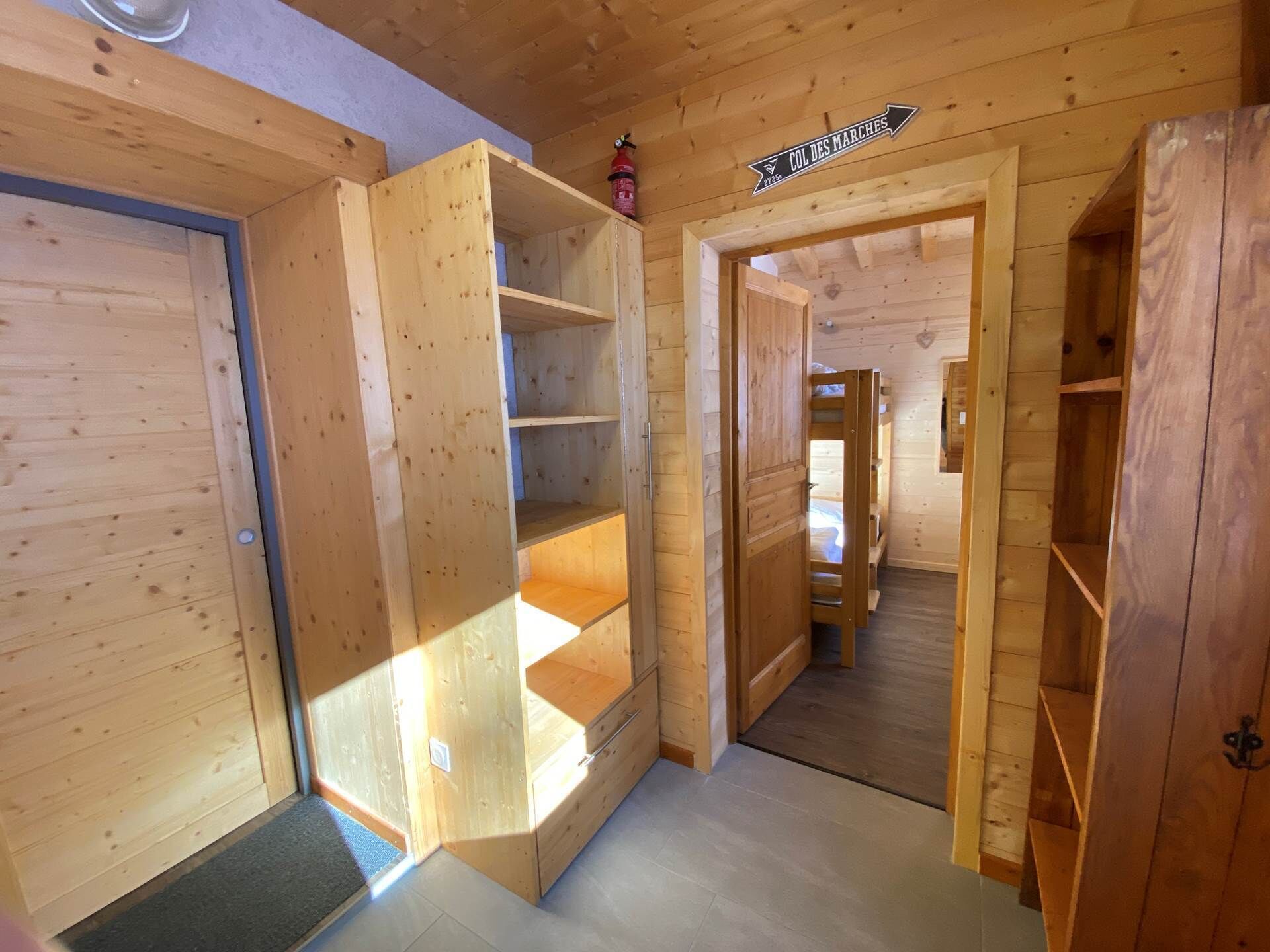 Interno in legno con un letto a castello, scaffali aperti e un cartello con la scritta “COL DES MARCHES”.