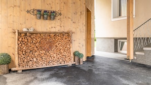 A wooden exterior wall with a stack of firewood, a metal shelf with potted plants, and a small decorative animal figure. - Centrally located holiday home with a garden (Zell am Ziller)