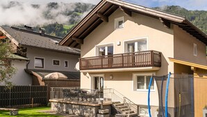 A two-story house with a balcony, a small garden, and a view of a forested mountain range. - Centrally located holiday home with a garden (Zell am Ziller)