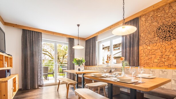A modern kitchen with wooden flooring, a dining table set for four, and a large window with curtains. - Centrally located holiday home with a garden (Zell am Ziller)