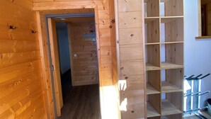 A wooden interior with a hallway leading to a room with a wooden shelf unit.