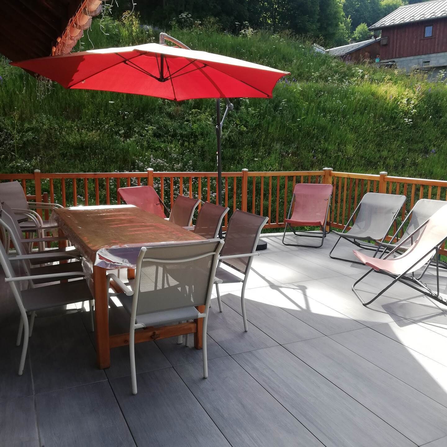 Un patio al aire libre con una mesa y sillas de madera, un paraguas rojo y una barandilla de madera.
