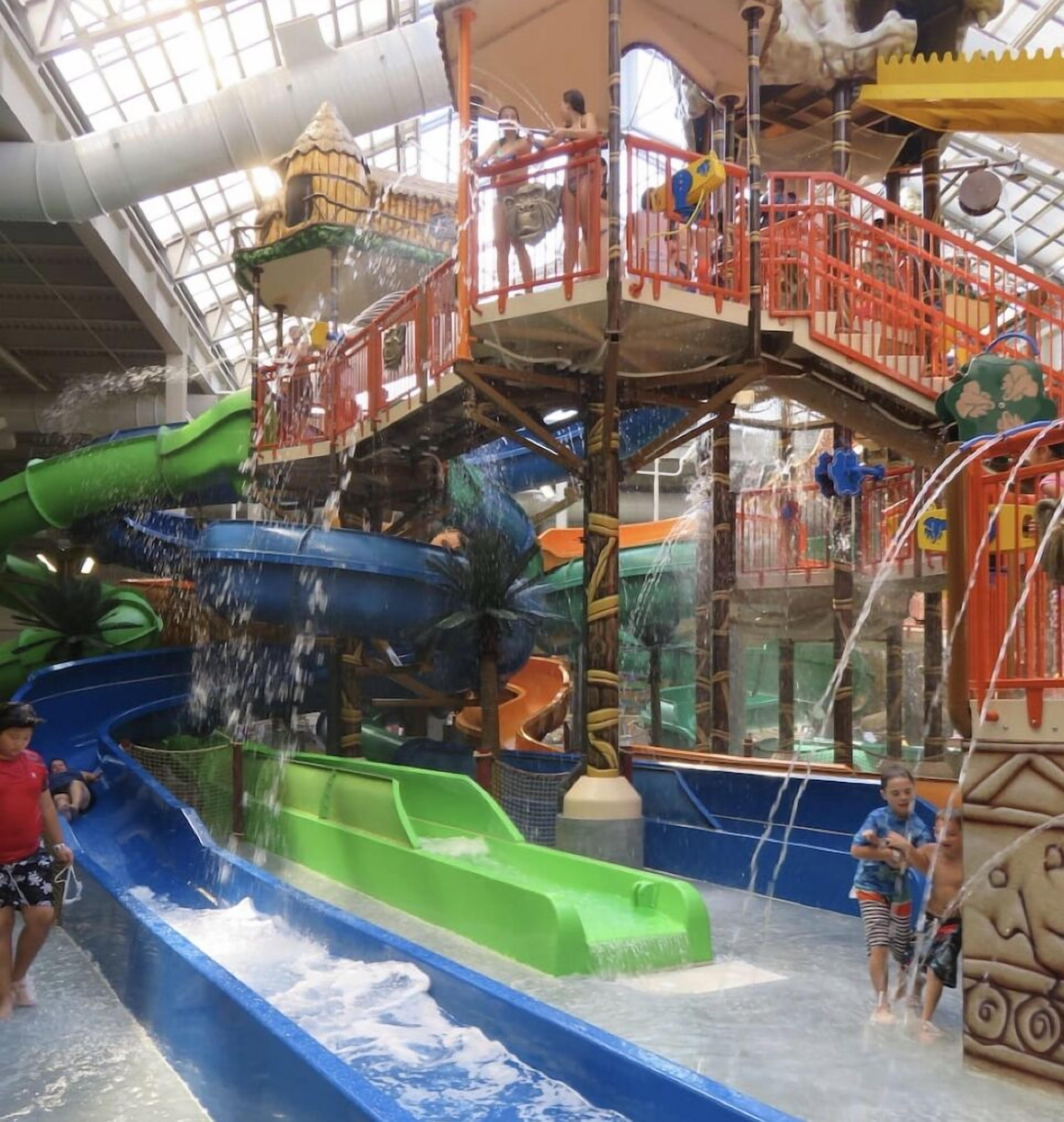 Een overdekt waterpark met meerdere glijbanen en een speelgebied in het midden.