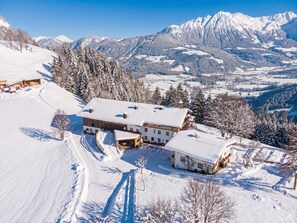 A snow-covered mountain resort with multiple buildings, including a large lodge and smaller cabins, surrounded by dense forests and snow-covered peaks. - Modern house with stunning views over the mountain world (Söll)