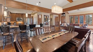 A spacious kitchen with wooden cabinets, a dining area with a long table and chairs, and a cozy living area with a sofa and windows. - Central to All Ski Areas, Private Hot Tub; Spacious Open Concept (Breckenridge)