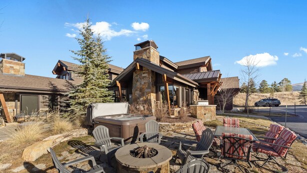 A stone fireplace surrounded by Adirondack chairs and a large stone table, with a stone chimney and a covered outdoor seating area. - Central to All Ski Areas, Private Hot Tub; Spacious Open Concept (Breckenridge)