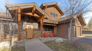 A modern log cabin with a stone foundation, wooden beams, and a covered porch with red Adirondack chairs. - Central to All Ski Areas, Private Hot Tub; Spacious Open Concept (Breckenridge)