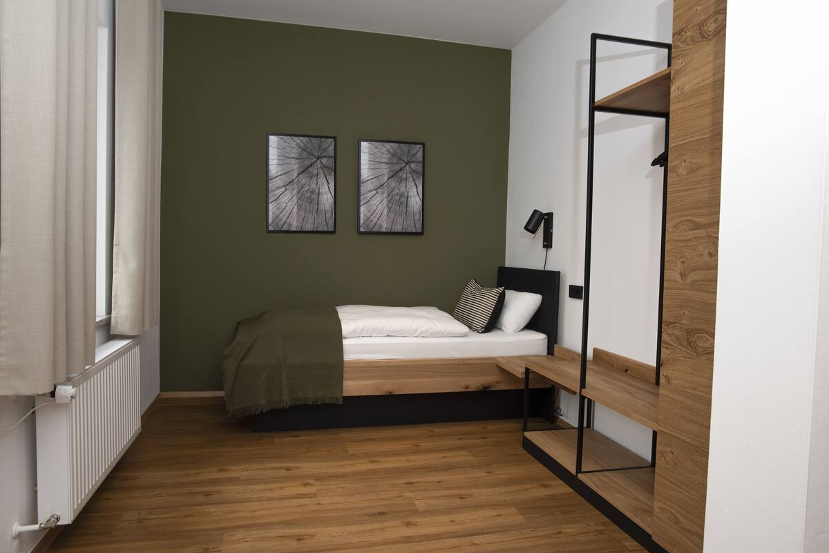 Une chambre à coucher comprenant un lit, un radiateur, une étagère et deux œuvres d’art abstraites accrochées au mur.