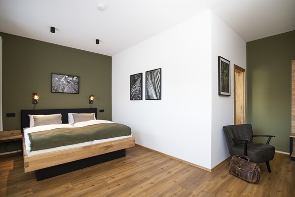 A modern bedroom with a wooden bed, green walls, and three framed pictures on the wall.