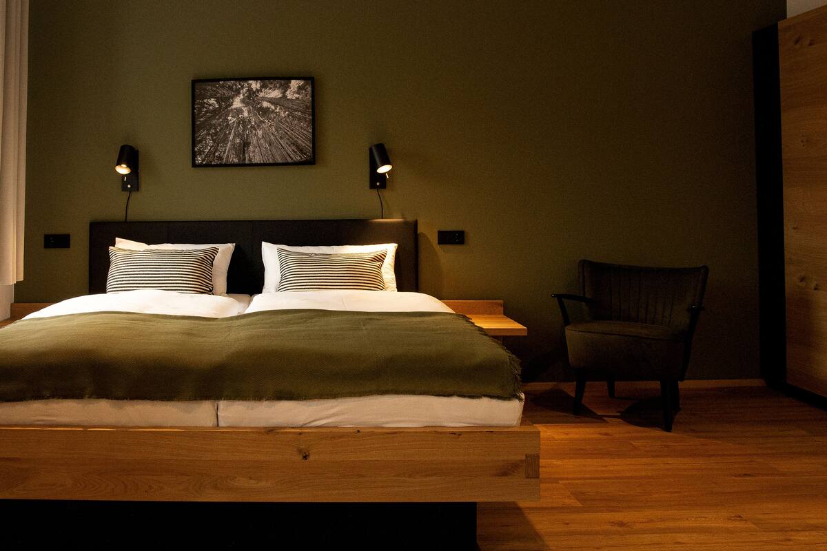 Une chambre à coucher avec un lit en bois, deux lampes de chevet, une chaise et un tableau encadré au mur.