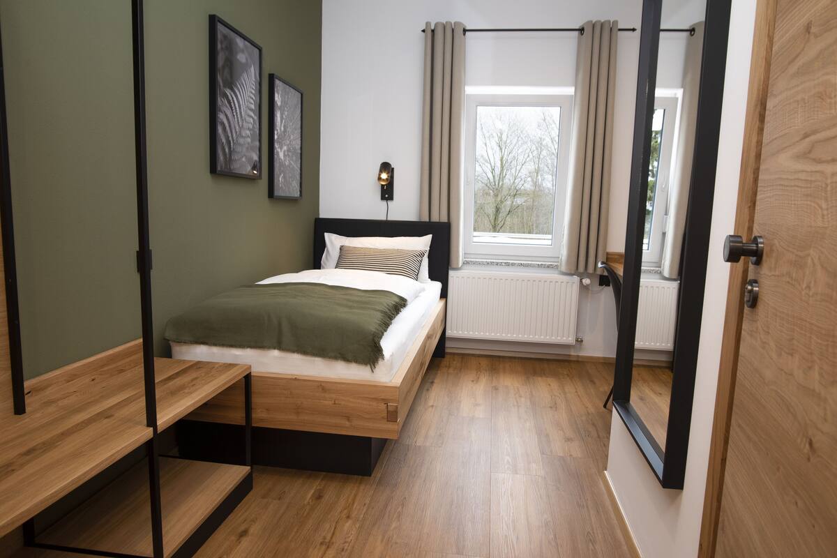 Une chambre à coucher avec un lit en bois, une table de chevet, une fenêtre avec des rideaux et un radiateur.
