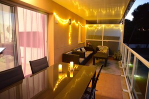A balcony with a glass railing, a dining table with candles, and string lights. - OFFRE SALOU  ONLY FAMILY   SEA VIEW LARGE TERRACE , POOLS  PARKING WIFI (Salou)