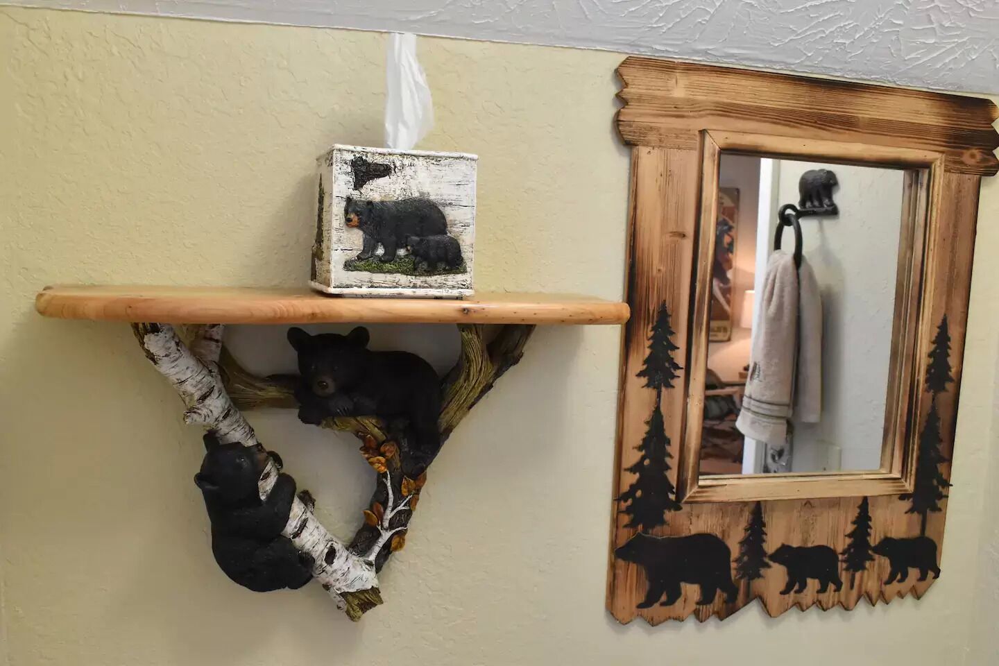 Un estante de pared con un adorno rústico con temática de oso, un espejo con marco en silueta de oso y una pequeña foto enmarcada.