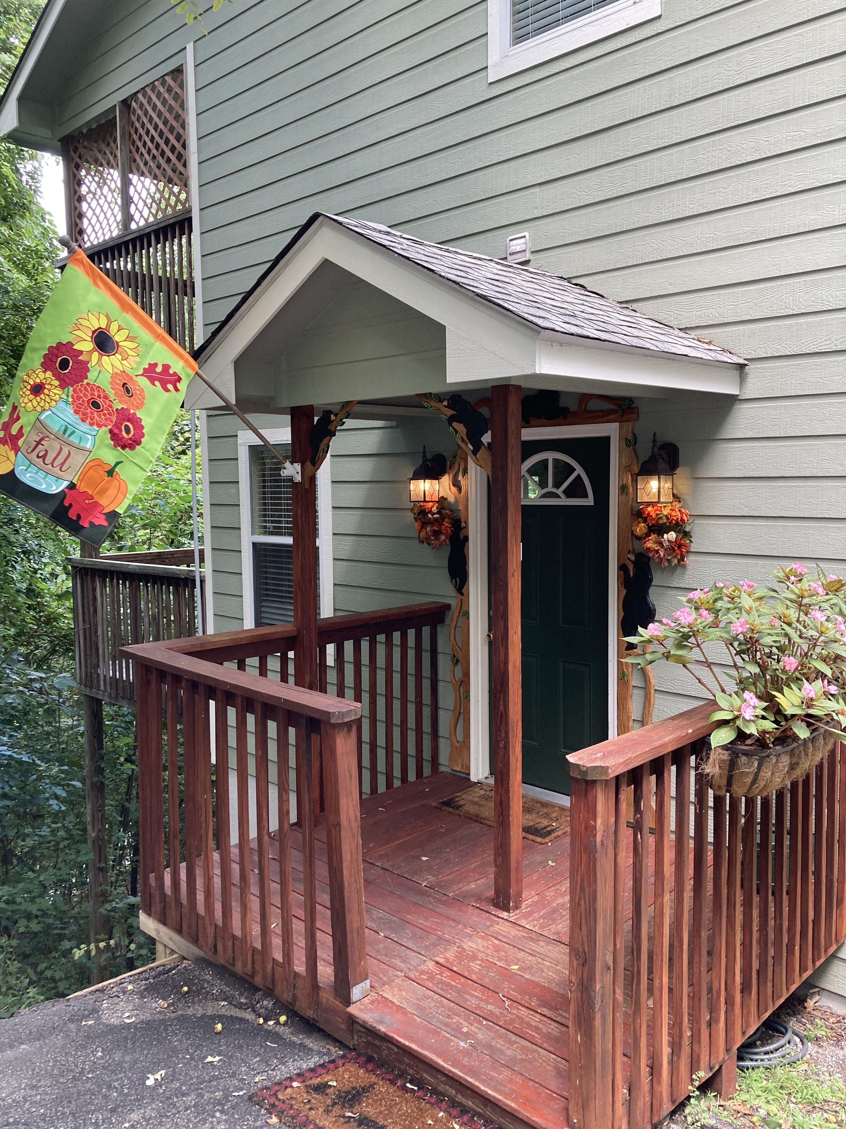 A wooden porch with a green door, a small covered area with a lantern, and a flower pot on the right.