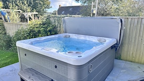 Un jacuzzi en un entorno al aire libre con una valla de madera y follaje de fondo.