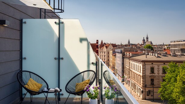 A balcony with two black wire-framed chairs, a glass partition, and potted plants. - Serviced Apartments G11 - between Main Market Square and Jewish Quarter by InPoint (Kraków)