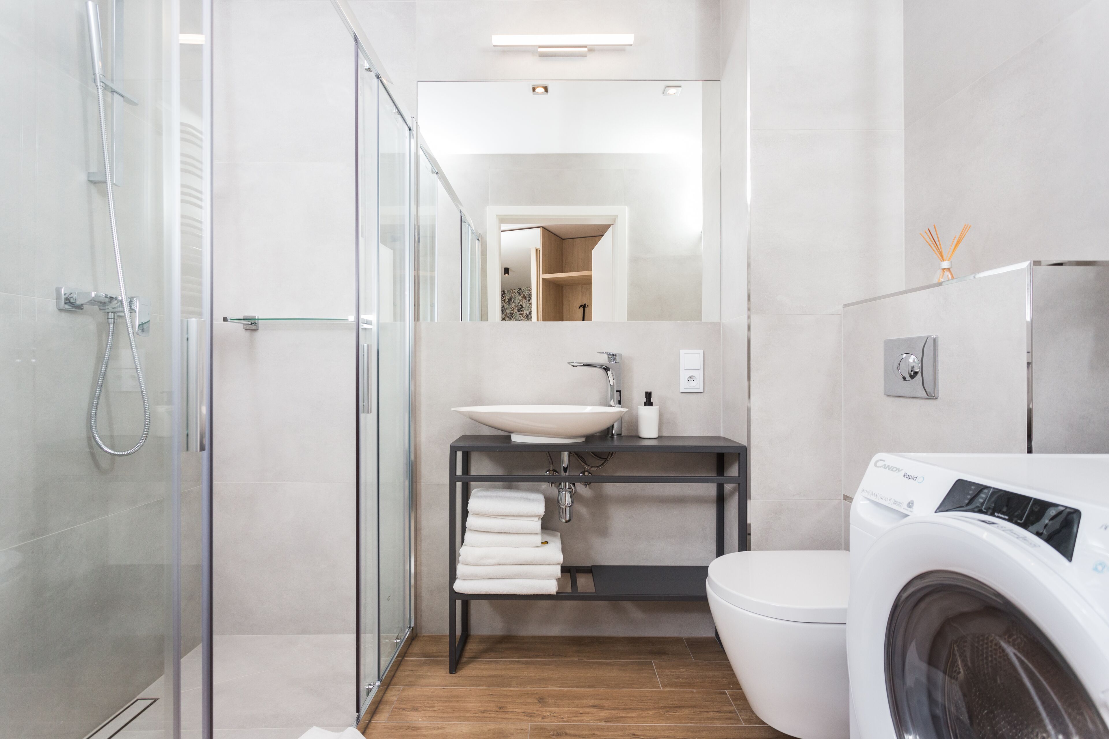 Ein modernes Badezimmer mit Duschkabine aus Glas, Waschbecken in Weiß, schwarzem Waschtisch, Toilette und einer Waschmaschine mit Frontlader.