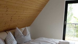A bedroom with a sloped ceiling, a large window, a bed with striped bedding, and pillows. - Pension Petersen (Bergen auf Ruegen)