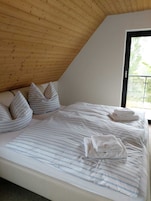 Un dormitorio con techo inclinado, un ventanal grande, una cama con ropa de cama a rayas y almohadas.