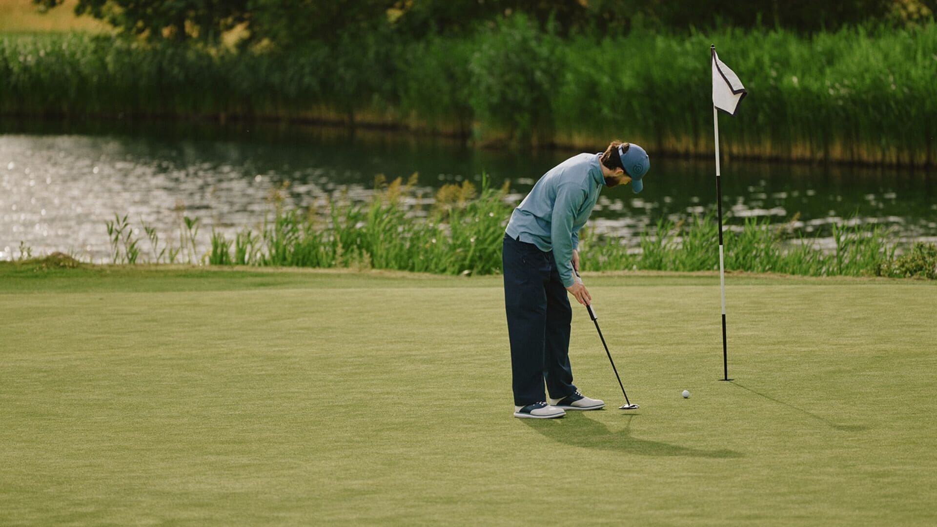 Un campo da golf con una bandiera, un green di putting e uno specchio d'acqua sullo sfondo.