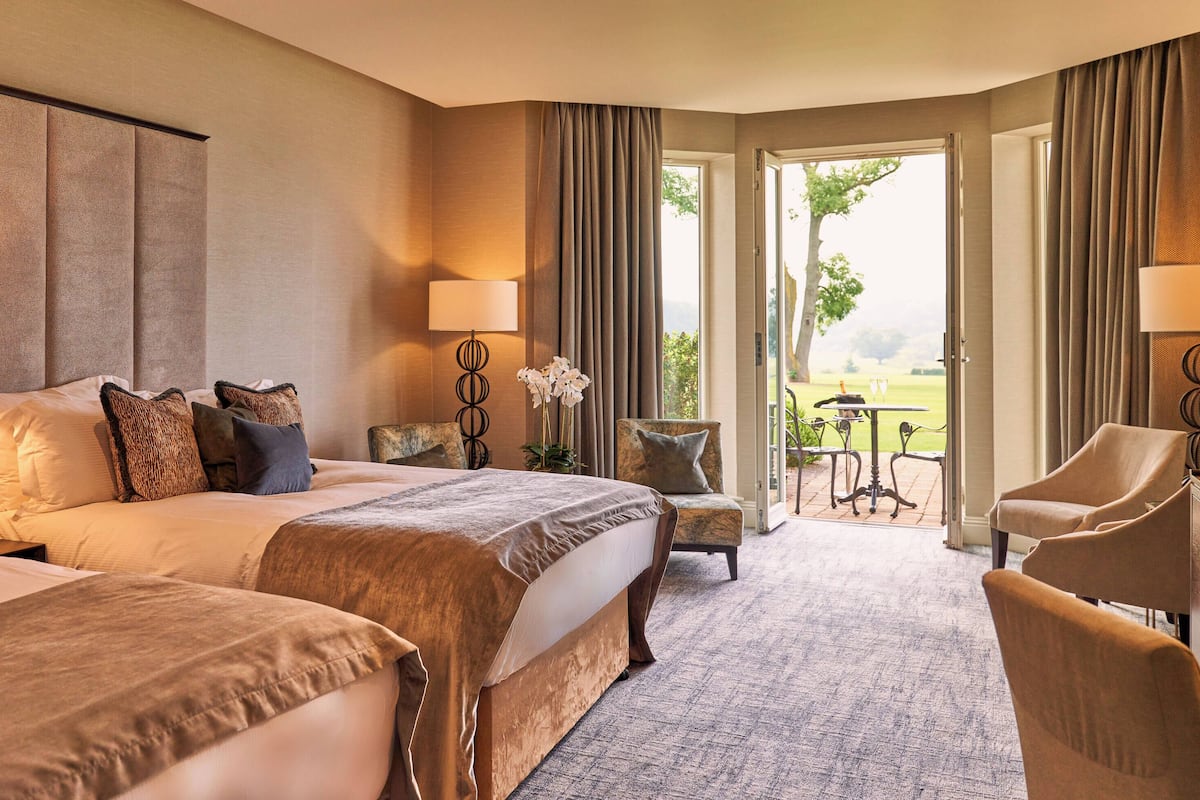 A hotel room with two beds, a sitting area with a chair, a table, and a view of the outdoors.