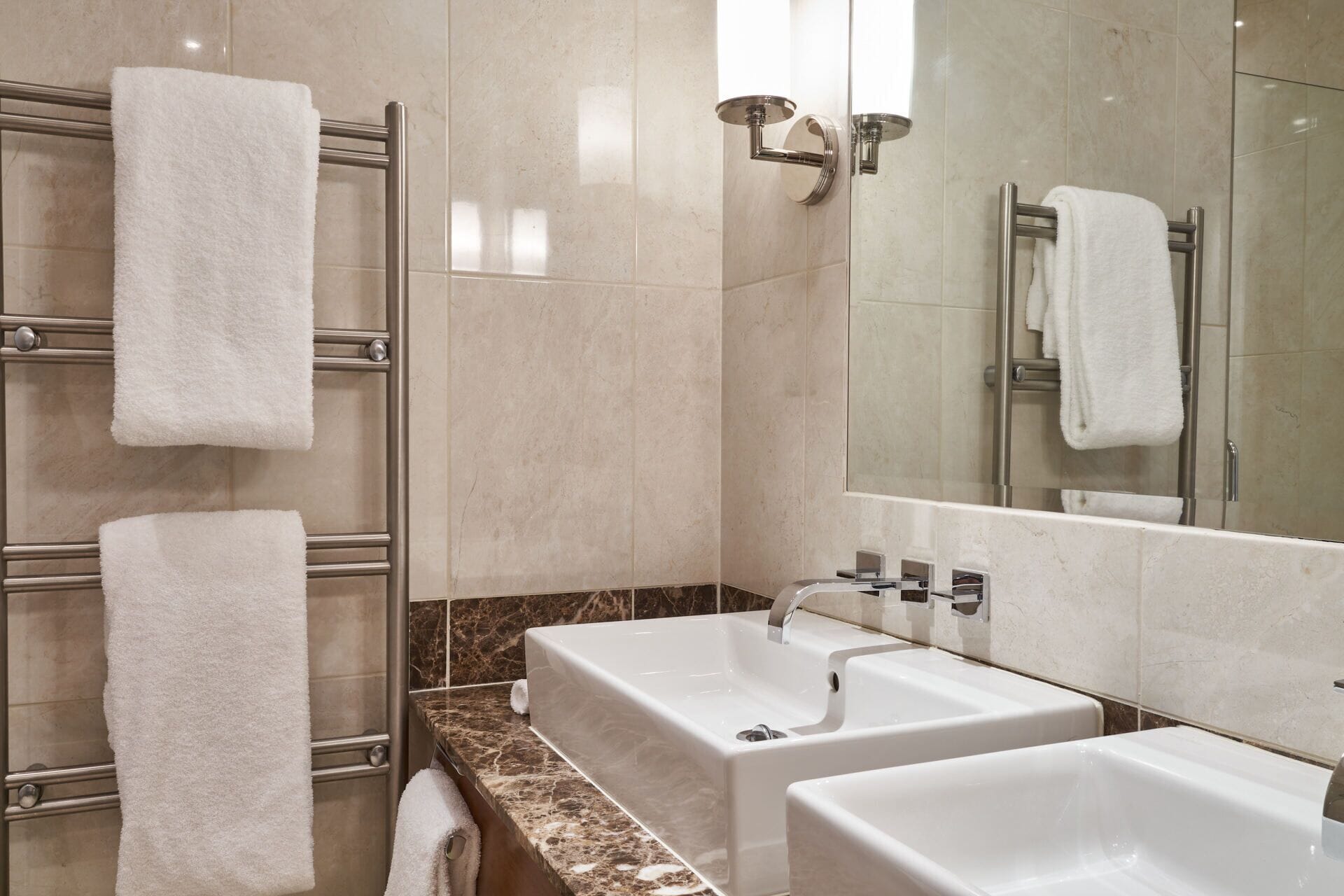 A modern bathroom with two sinks, a glass shower enclosure, and a towel rack with multiple towels.