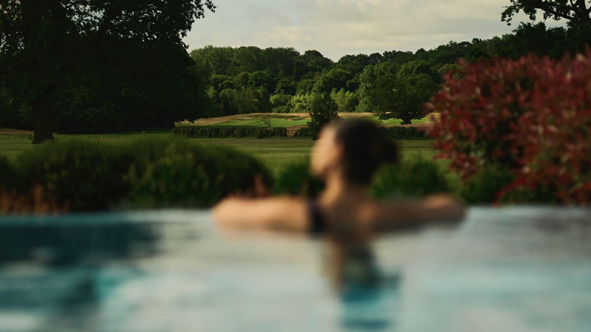 A person in a swimming pool with a blurred background of greenery and trees.