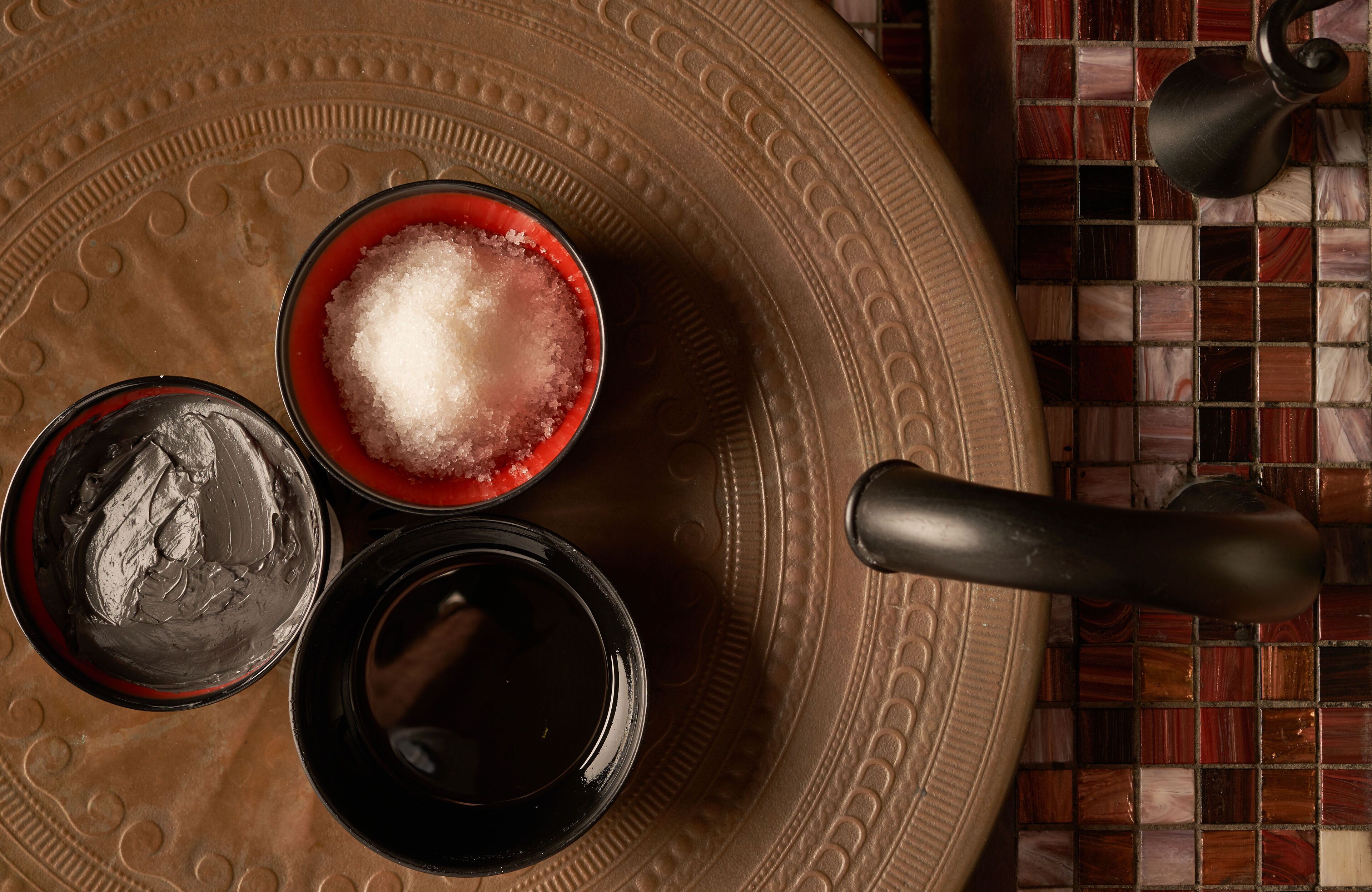 A tray with three bowls containing different substances, a spoon, and a tiled wall in the background.