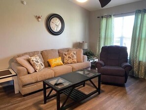 A living room with a sofa, armchair, coffee table, wall clock, and a lamp. - Cozy Broken Arrow Home -- Special Pricing for 30+ day stays! (Broken Arrow)